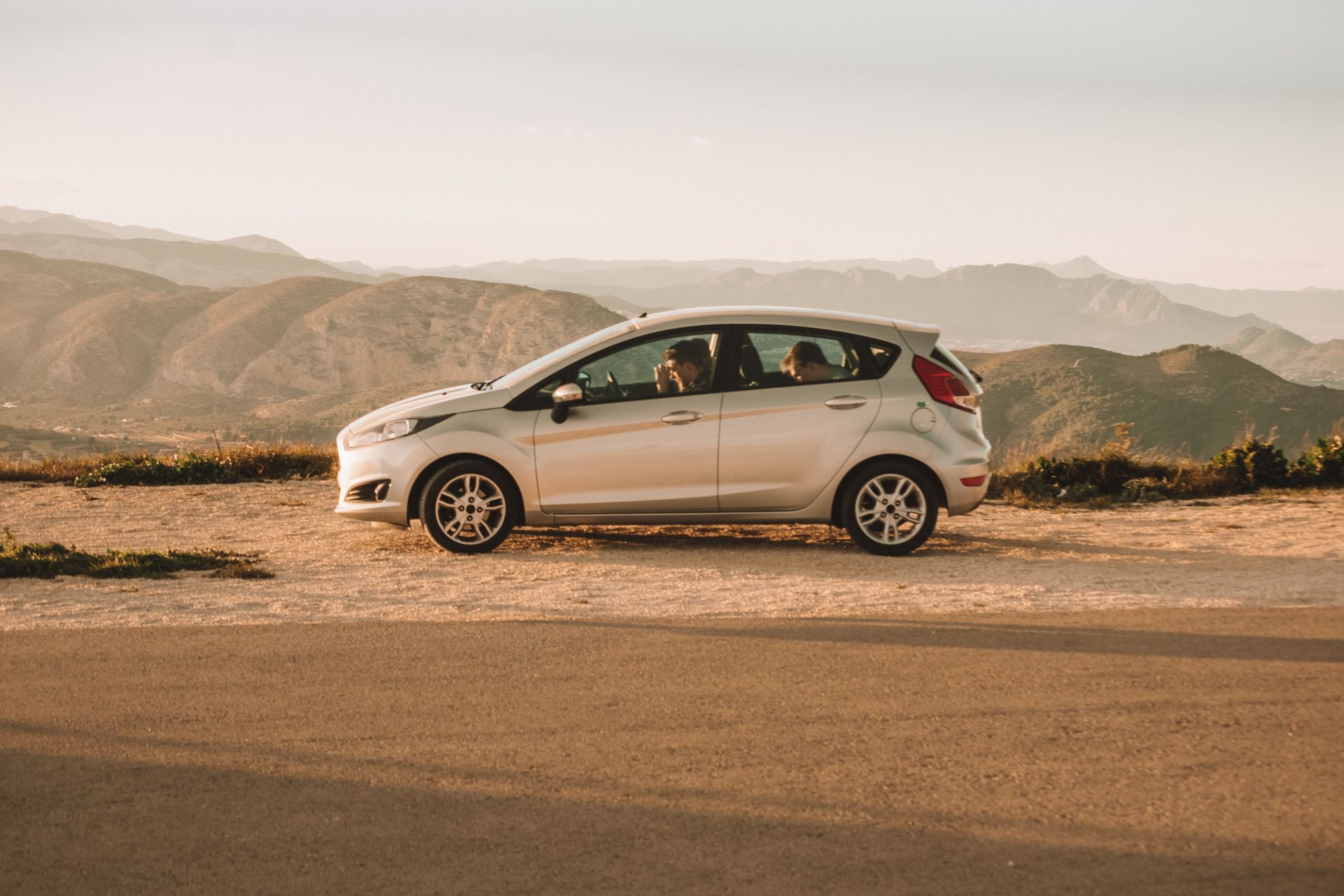 A parked car beside a road with stunning mountainous backdrop in Spain, capturing a serene and picturesque road trip moment.